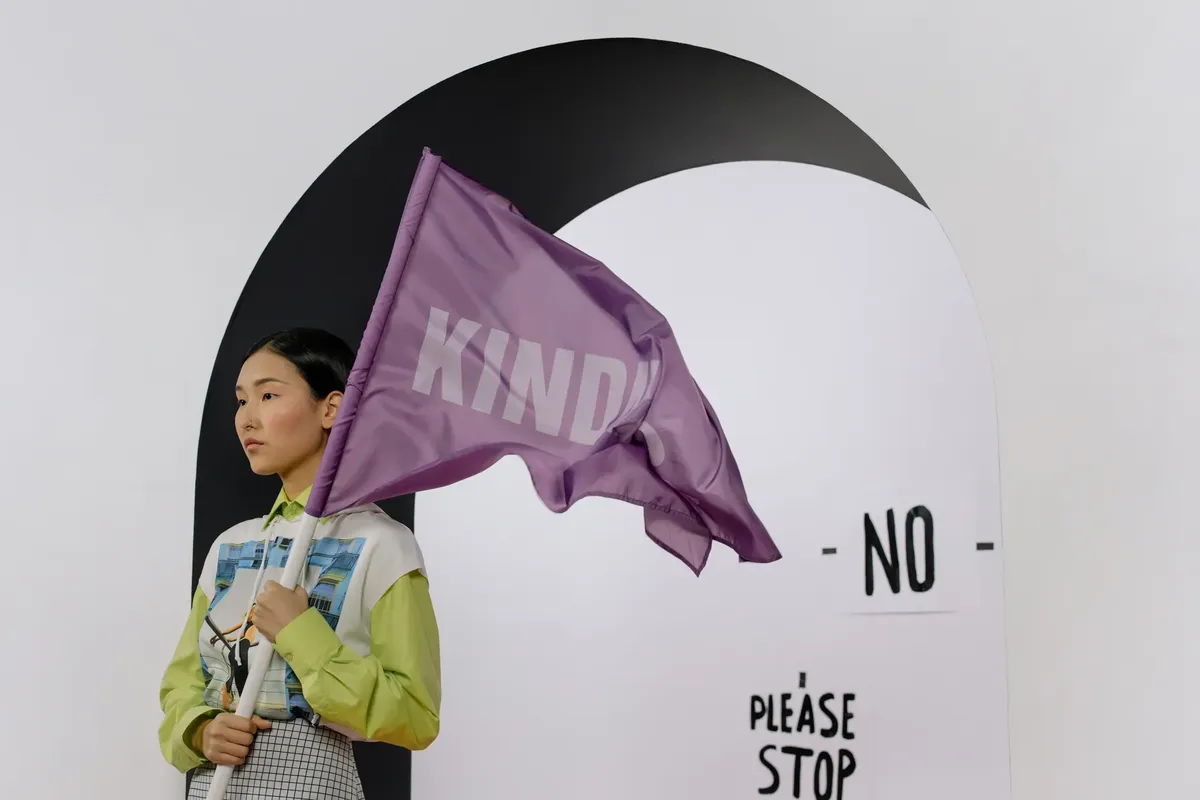 Asian woman with purple 'KIND' flag in modern indoor setup.
